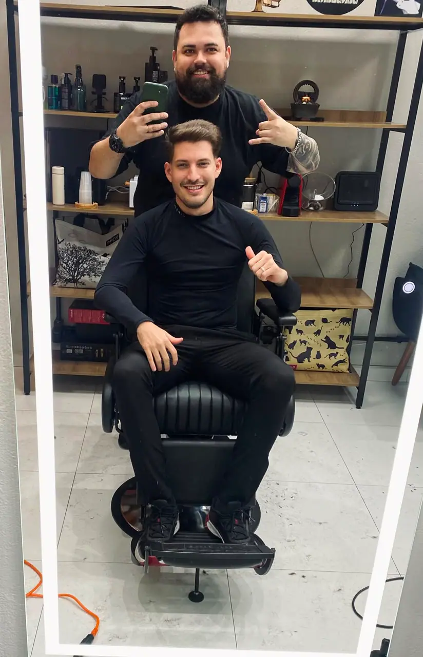 Cliente sorrindo na cadeira com o corte finalizado, ao lado do barbeiro